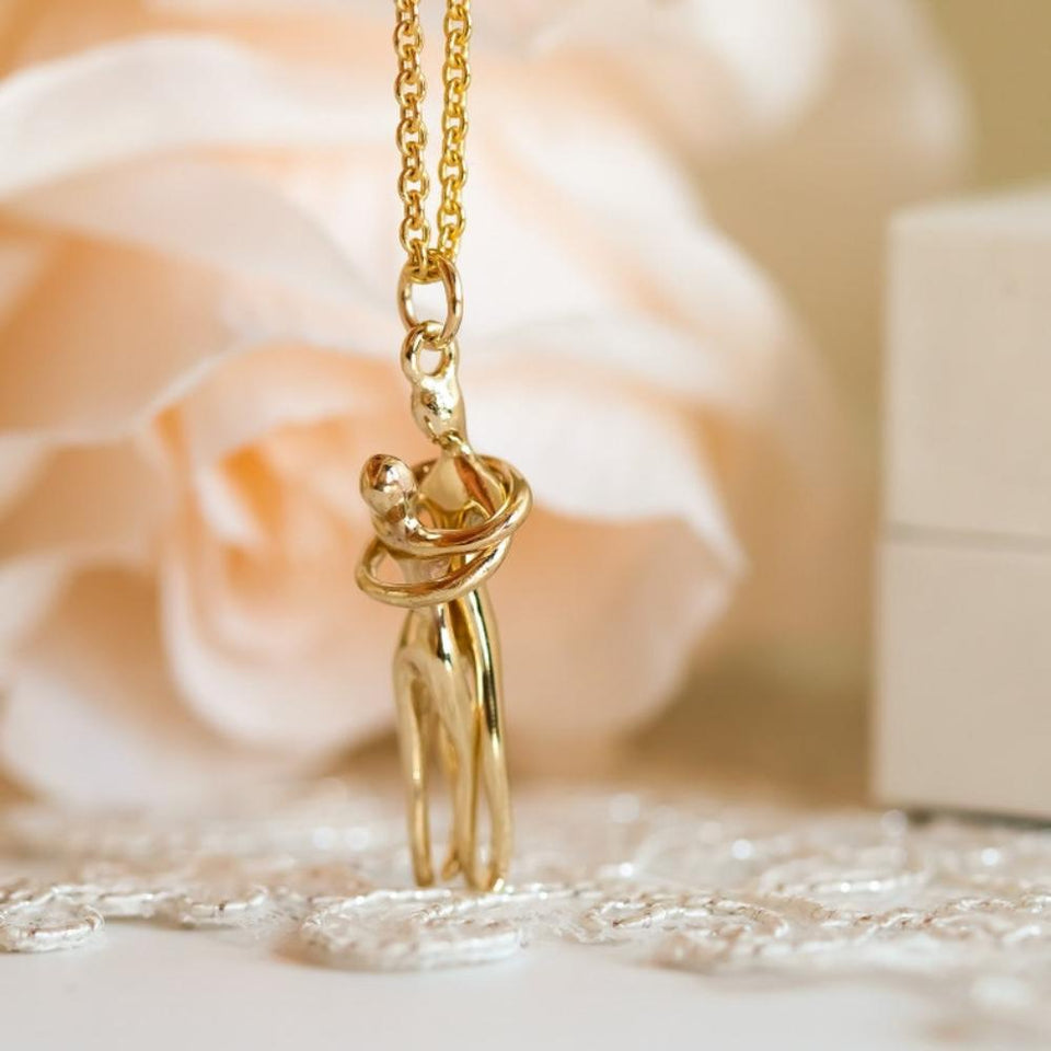 Hug Necklace in gold color in front of a stylized background